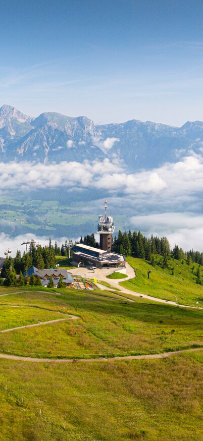 Blick von der Planai über grüne Landschaft auf das Dachsteinmassiv mit Wolken und Fernsicht | © Josh Absenger